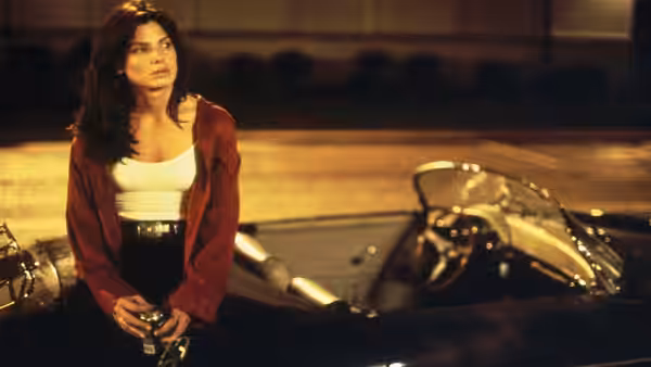 A woman in a red cardigan leans against a motorcycle, holding a bottle