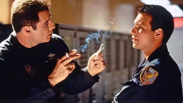 Two airmen talk inside a military facility, one holding a cigarette