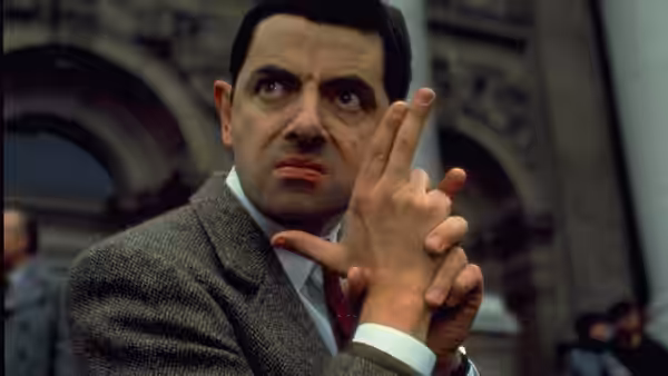 Mr. Bean (Rowan Atkinson) clasps his hands on a city street