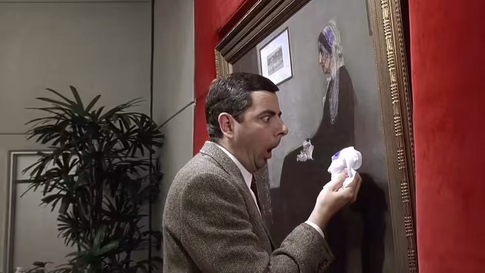 Mr. Bean (Rowan Atkinson) holds a tissue beside a framed painting in a gallery