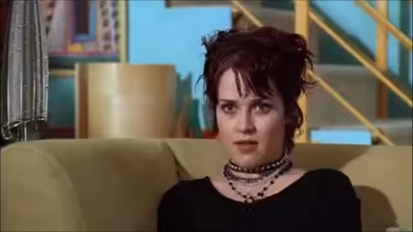 A woman in a black top sits on a sofa indoors