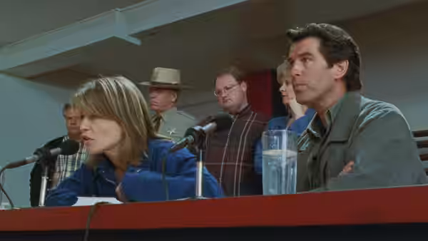 Rachel Wando (Linda Hamilton) speaks at a press conference beside Harry Dalton (Pierce Brosnan)