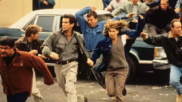 Harry Dalton (Pierce Brosnan) and Rachel Wando (Linda Hamilton) flee through a street as people run