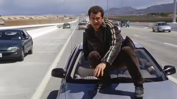 Martin Riggs (Mel Gibson) crouches atop a moving car on a busy highway