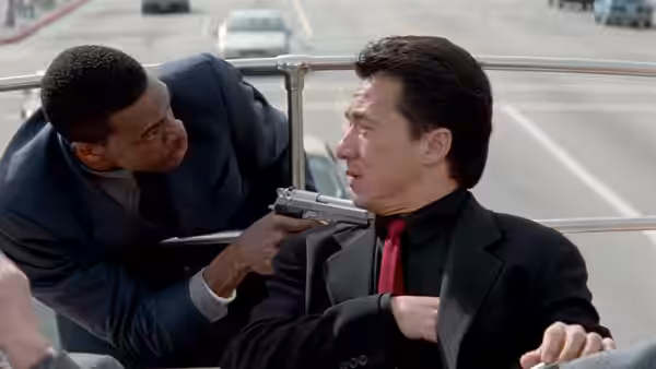 Carter (Chris Tucker) leans over Lee (Jackie Chan), holding a gun beside his neck