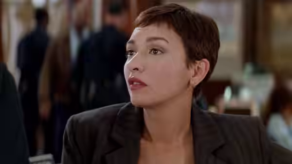 A short-haired woman in a dark suit looks up from a table in a restaurant