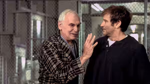 Patch Adams (Robin Williams) listens as an older man gestures in a fenced institutional room