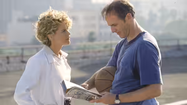 Maggie (Meg Ryan) talks with a man holding a basketball and booklet