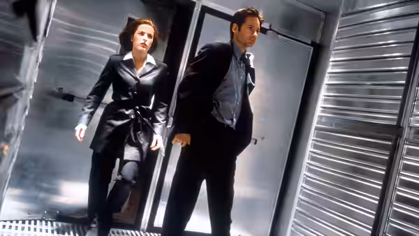 Dana Scully (Gillian Anderson) and Fox Mulder (David Duchovny) walk through a metal corridor