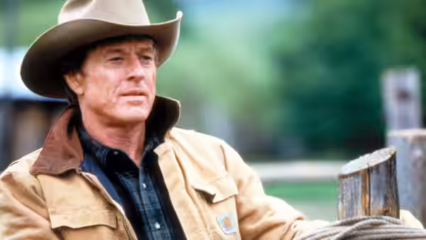 Tom Booker (Robert Redford) leans beside a wooden fence at the ranch