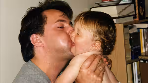 A man kisses a toddler while holding the child close indoors