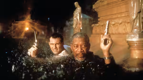 Jim (Morgan Freeman) and Tom (Christian Slater) wade through floodwater beside a stone building