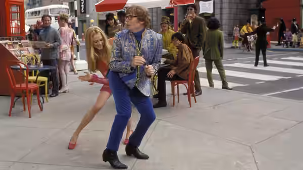 Austin Powers dances on a city sidewalk as Felicity Shagwell moves behind him