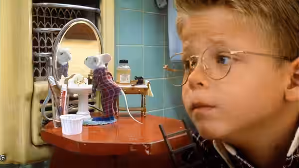 George watches Stuart brush his teeth at a tiny bathroom sink