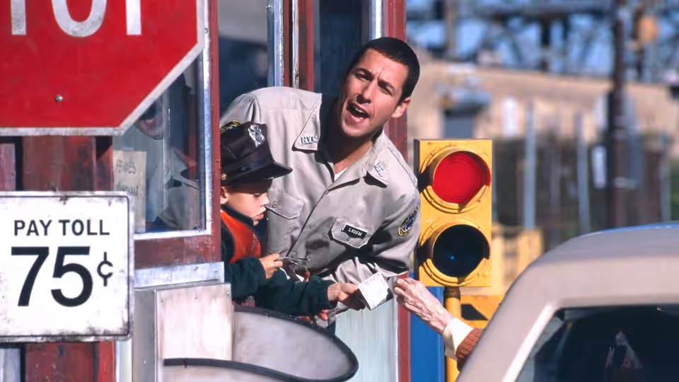 Sonny (Adam Sandler) leans from a tollbooth beside Julian dressed as a police officer