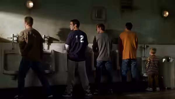 Sonny and Julian stand among men using sinks in a public restroom