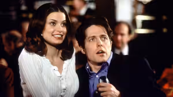 Gina Vitale (Jeanne Tripplehorn) and Michael Felgate (Hugh Grant) watch something together at a crowded event