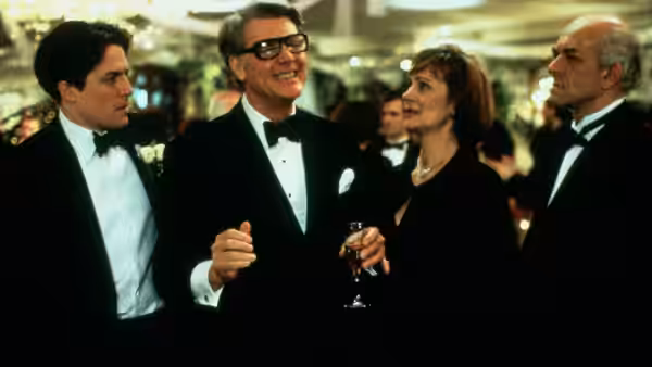 Michael Felgate (Hugh Grant) stands with formally dressed guests at a reception