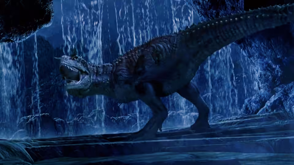 A large predatory dinosaur prowls through a rocky cavern beneath cascading water