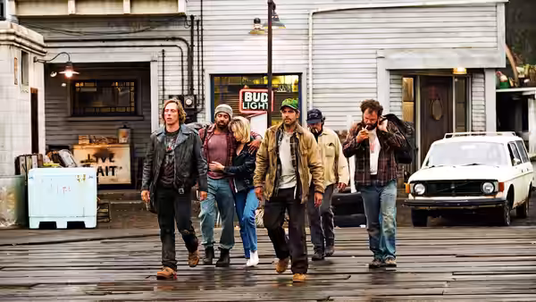 A group of fishermen walk along a wet street past a bar and parked car