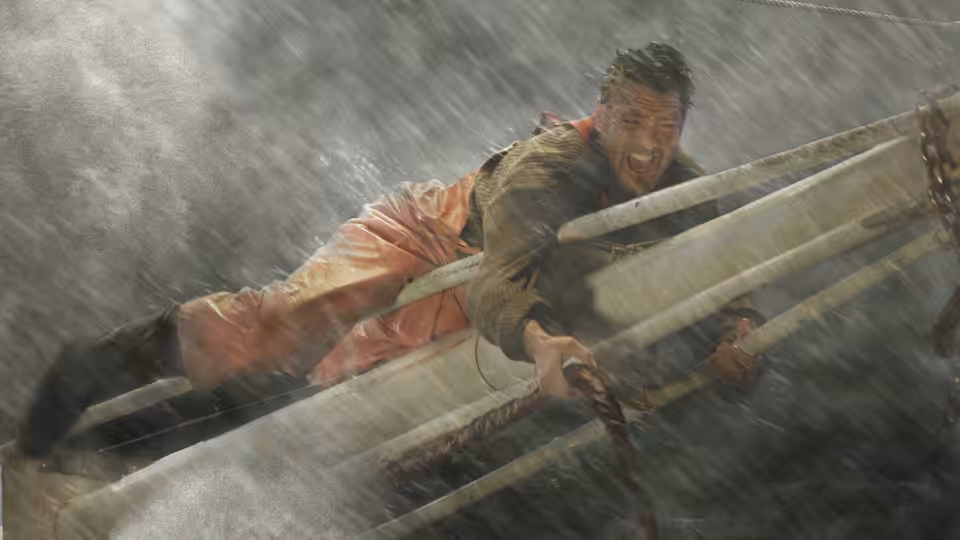 A fisherman in orange waterproofs clings to the rail of a boat in driving rain