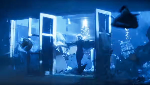 A figure struggles amid shattered glass and water in a flooded enclosure