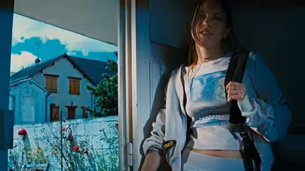 A woman with a shoulder bag stands in a doorway beside a house