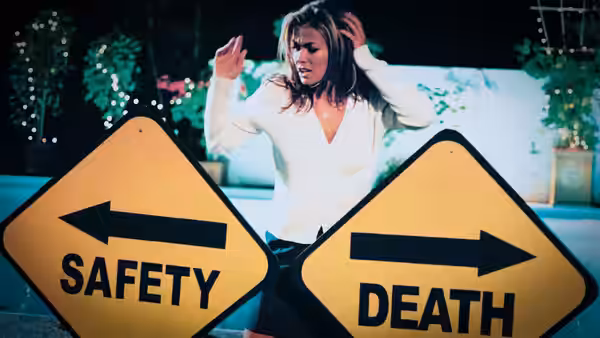 A woman raises her hands between roadside signs pointing toward safety and death