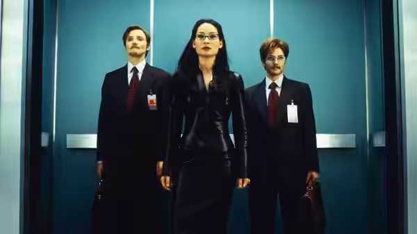 Alex Munday (Lucy Liu) strides through an elevator between two suited men