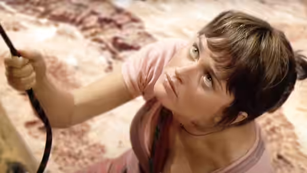 A young woman in a pink shirt looks upward while gripping a climbing rope