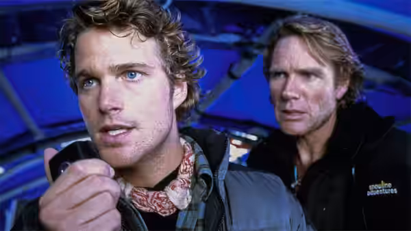 Peter Garrett (Chris O'Donnell) speaks into a radio while a man stands behind him indoors