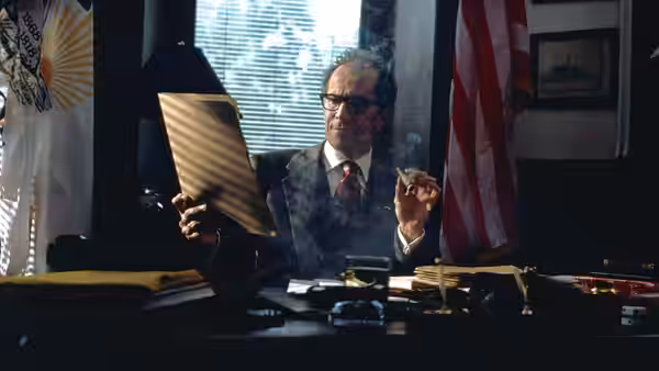 Shelly Runyon (Gary Oldman) examines a folder at his desk amid cigarette smoke