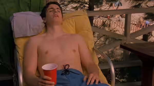 Jim Levenstein reclines shirtless on a deck chair, holding a red cup