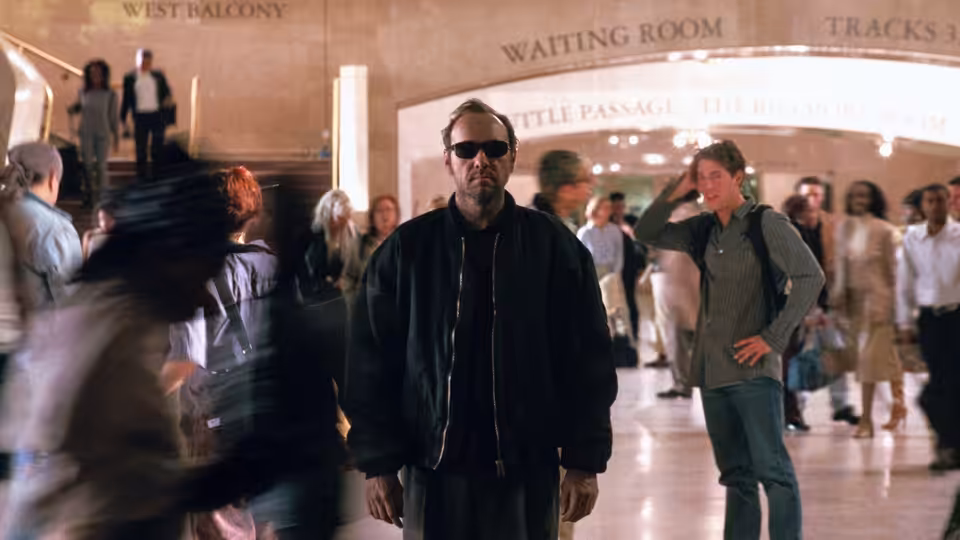 Prot (Kevin Spacey) stands in sunglasses in a crowded railway station