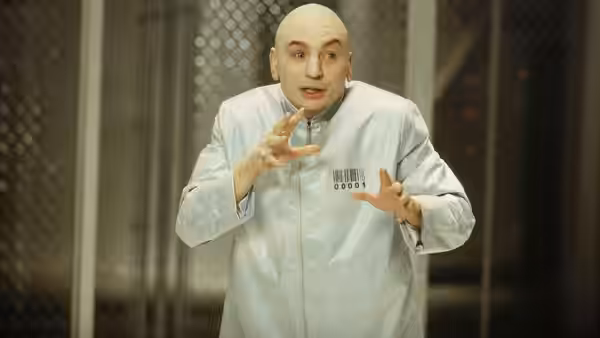 Dr. Evil (Mike Myers) gestures inside a light-blue prison uniform behind a mesh partition
