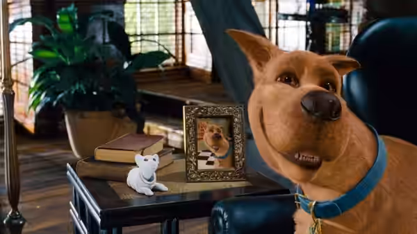 Scooby-Doo sits beside a framed portrait and a small white dog figurine