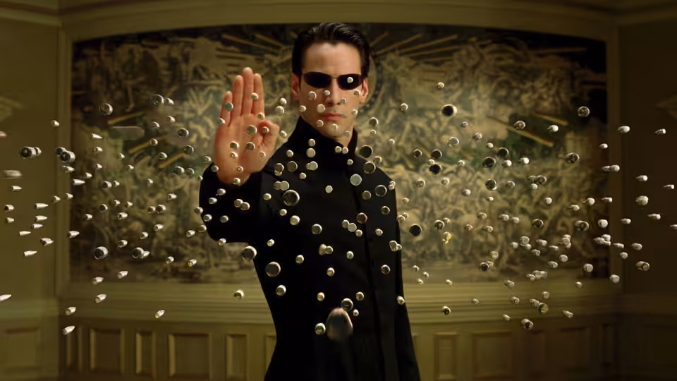 Neo (Keanu Reeves) holds bullets suspended before him in an ornate room