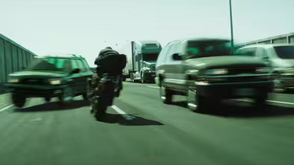 Trinity (Carrie-Anne Moss) rides a motorcycle between vehicles on a highway