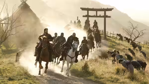 Samurai riders charge down a dusty village road beneath a wooden gate