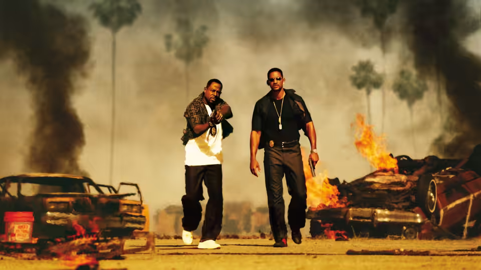 Detectives Marcus Burnett (Martin Lawrence) and Mike Lowrey (Will Smith) walk between burning cars