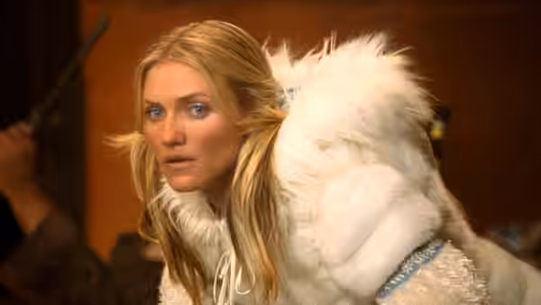 A blonde woman in a white fur coat looks over her shoulder indoors
