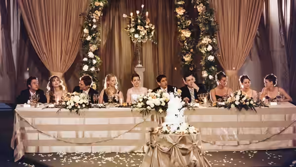 A wedding party sits behind a flower-covered head table beneath floral arches