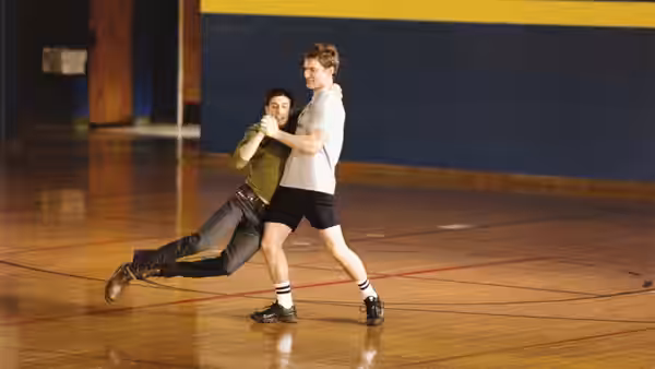 Two men grapple playfully on a gymnasium floor