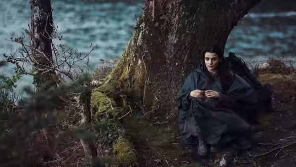 woman in dark clothing sitting on the ground beside a tree