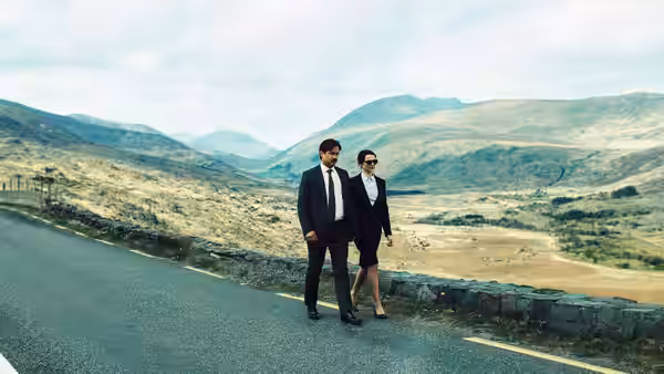 man and woman standing on a mountain road overlooking a valley