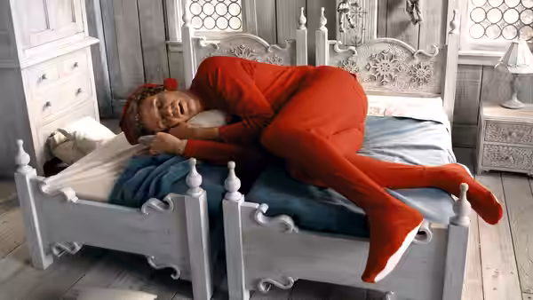 Buddy (Will Ferrell) curls up across a small bed in his elf home