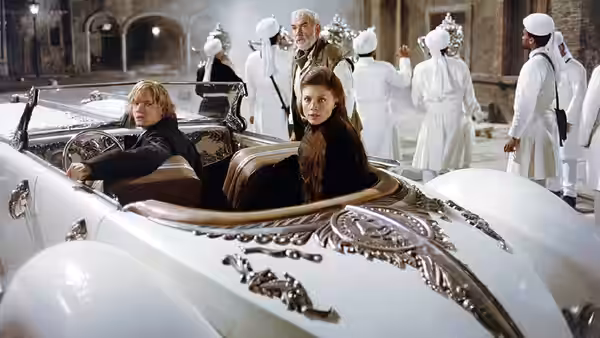 Tom Sawyer (Shane West) and Mina Harker (Peta Wilson) sit in an ornate car as white-clad attendants gather