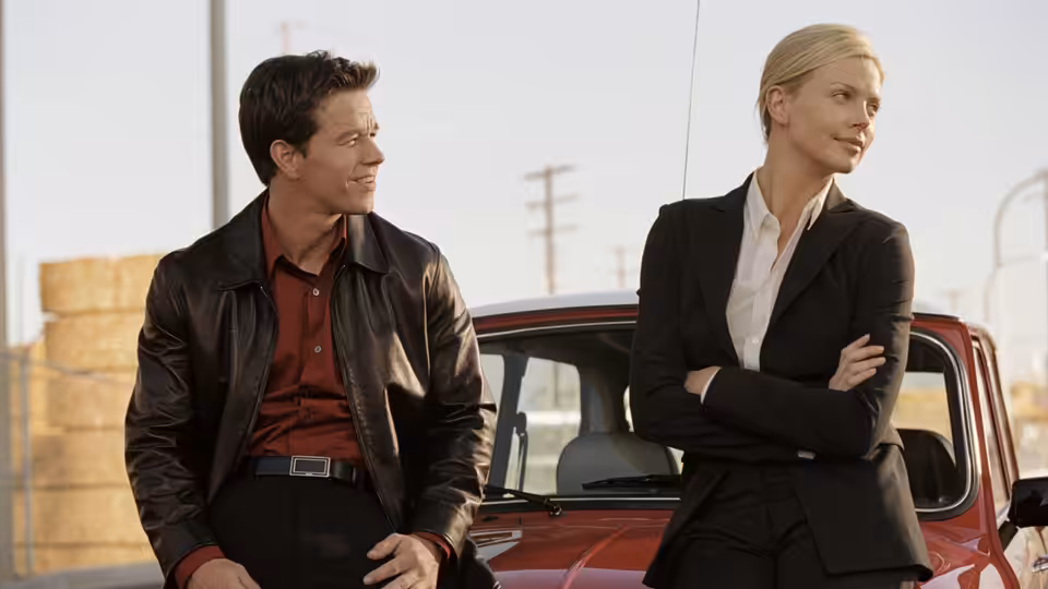 Charlie Croker (Mark Wahlberg) and Stella Bridger (Charlize Theron) stand beside a red car