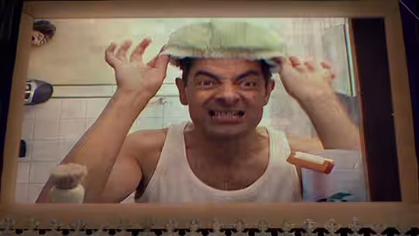 Johnny English (Rowan Atkinson) grimaces while adjusting a shower cap in a bathroom mirror
