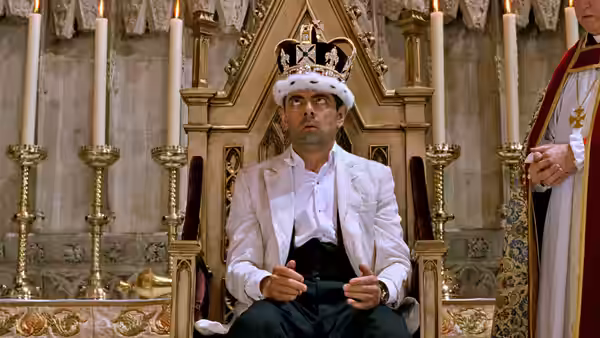 Johnny English (Rowan Atkinson) sits on a throne wearing a crown and white robes